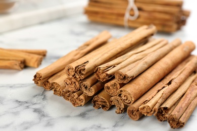 Aromatic cinnamon sticks on white marble table, closeup