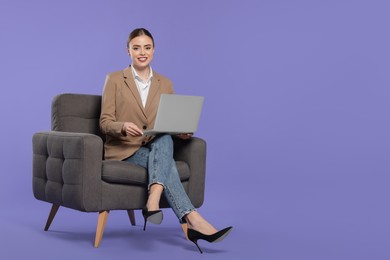 Happy woman with laptop sitting in armchair on violet background. Space for text