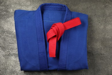 Photo of Red karate belt and blue kimono on gray textured background, top view