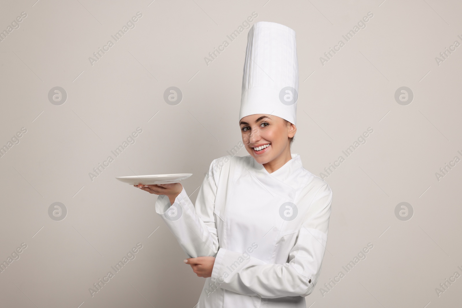 Photo of Happy professional confectioner in uniform holding empty plate on light grey background