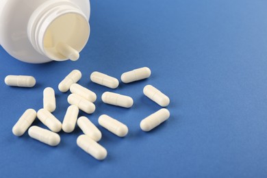 Bottle and vitamin capsules on blue background, closeup. Space for text