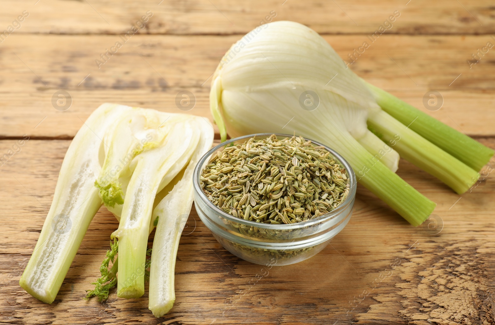 Photo of Fennel seeds in bowl and fresh vegetables on wooden table, closeup