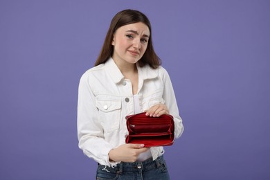 Sad woman showing empty wallet on purple background