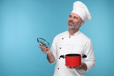Happy chef in uniform with cooking pot on light blue background, space for text