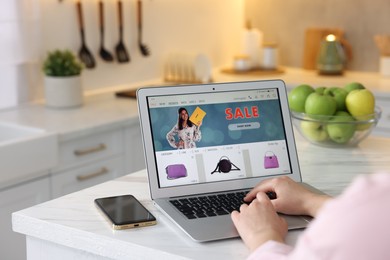 Photo of Woman shopping online during sale on laptop in kitchen, closeup
