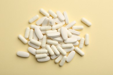 Photo of Vitamin pills on pale yellow background, flat lay