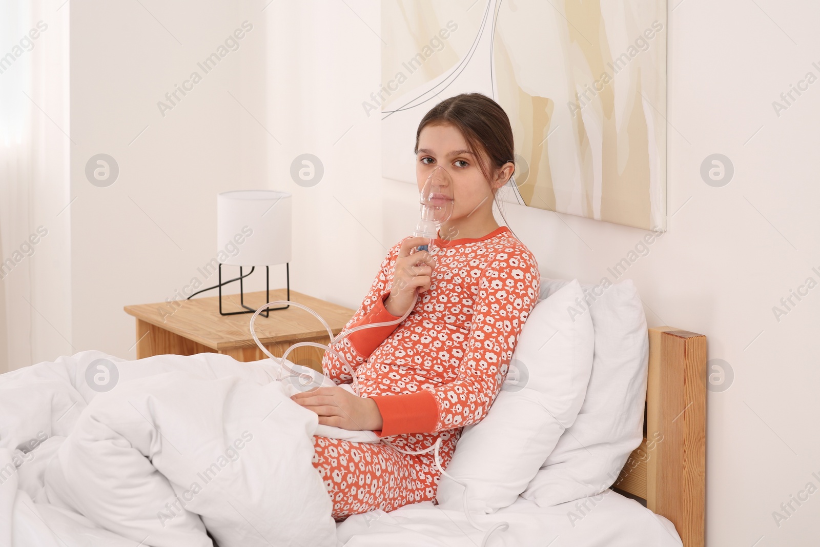 Photo of Cute girl using nebulizer for inhalation on bed at home