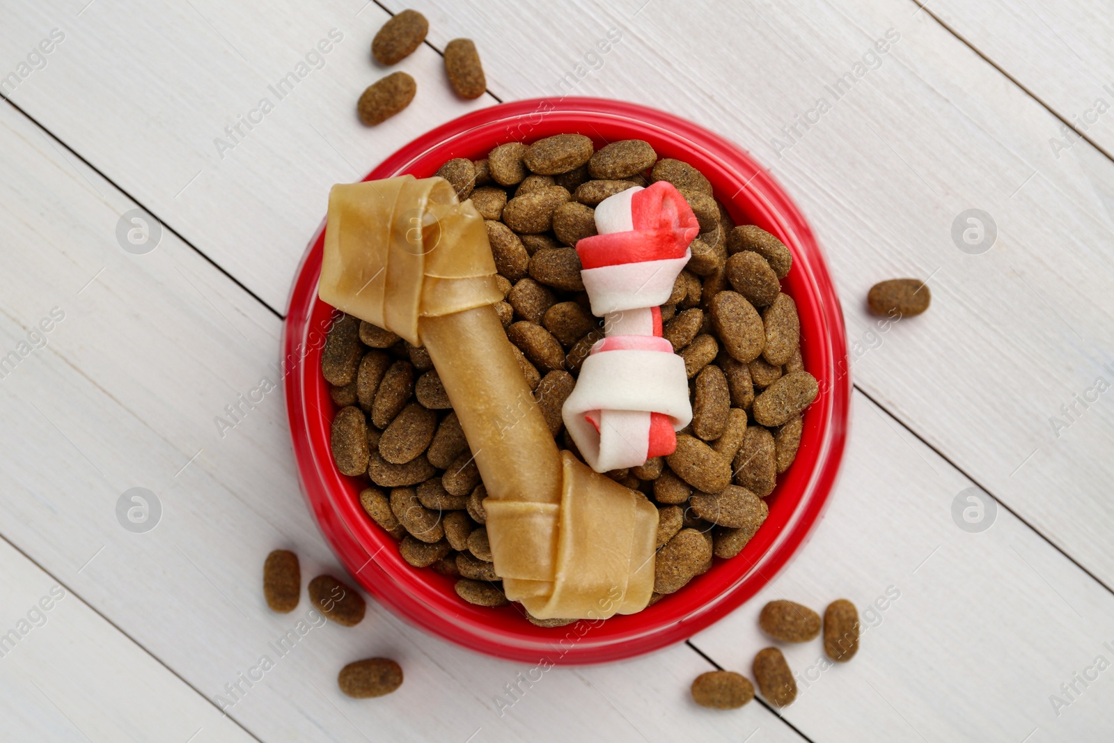 Photo of Dry dog food and treats (chew bones) on white wooden floor, flat lay