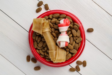 Dry dog food and treats (chew bones) on white wooden floor, flat lay