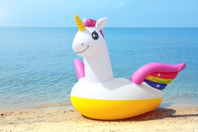 Photo of Funny inflatable unicorn ring on sandy beach near sea. Space for text