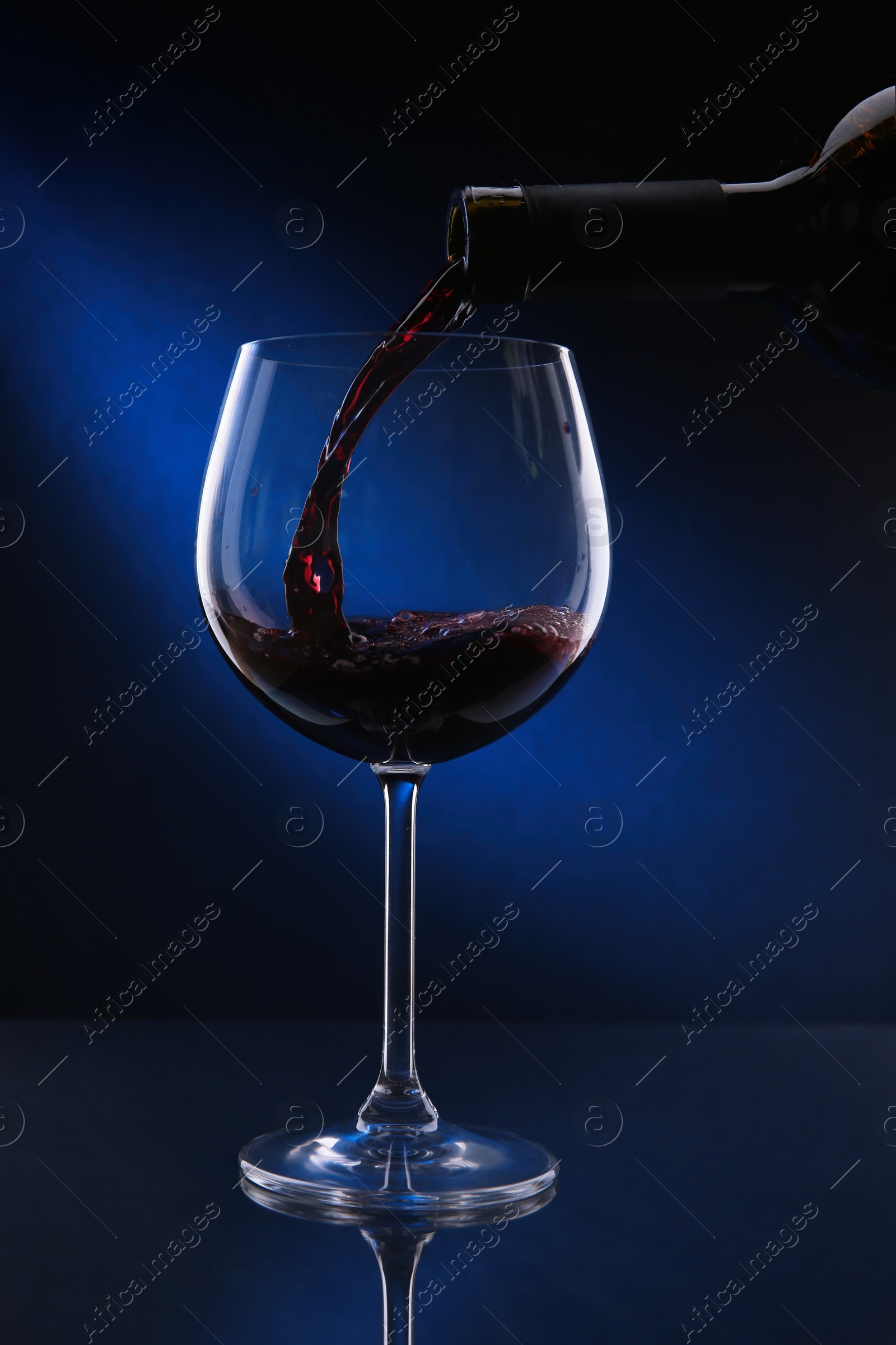 Photo of Pouring red wine from bottle into glass on color background