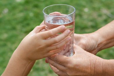 Child giving glass of water to elderly woman outdoors, closeup