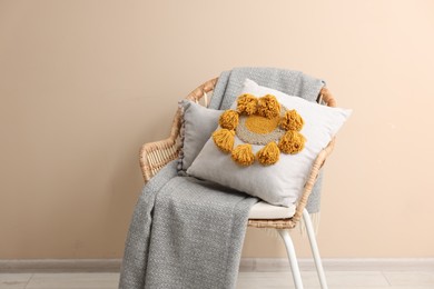 Photo of Stylish soft pillow and blanket on armchair near beige wall indoors