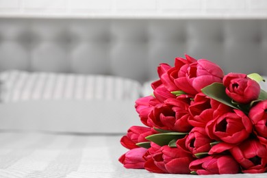 Photo of Many beautiful tulips on bed at home. Space for text