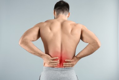 Image of Young man suffering from back pain on light background