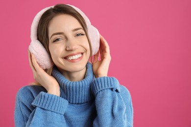 Photo of Happy woman wearing warm earmuffs on pink background, space for text