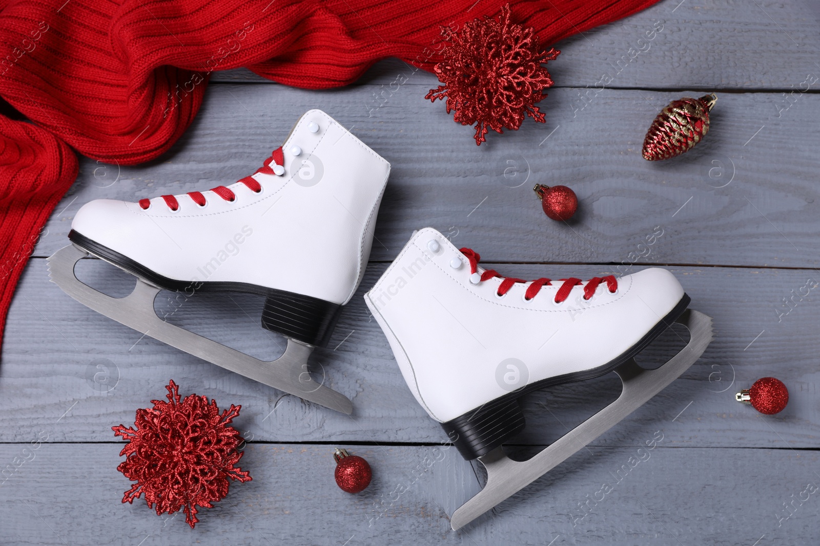 Photo of Pair of ice skates, Christmas decor and red scarf on grey wooden background, flat lay