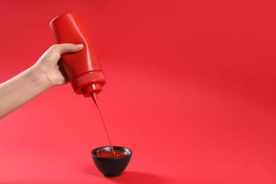 Woman pouring tasty ketchup from bottle into bowl on red background, closeup. Space for text