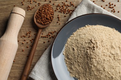 Photo of Plate with buckwheat flour, grains and rolling pin on wooden table