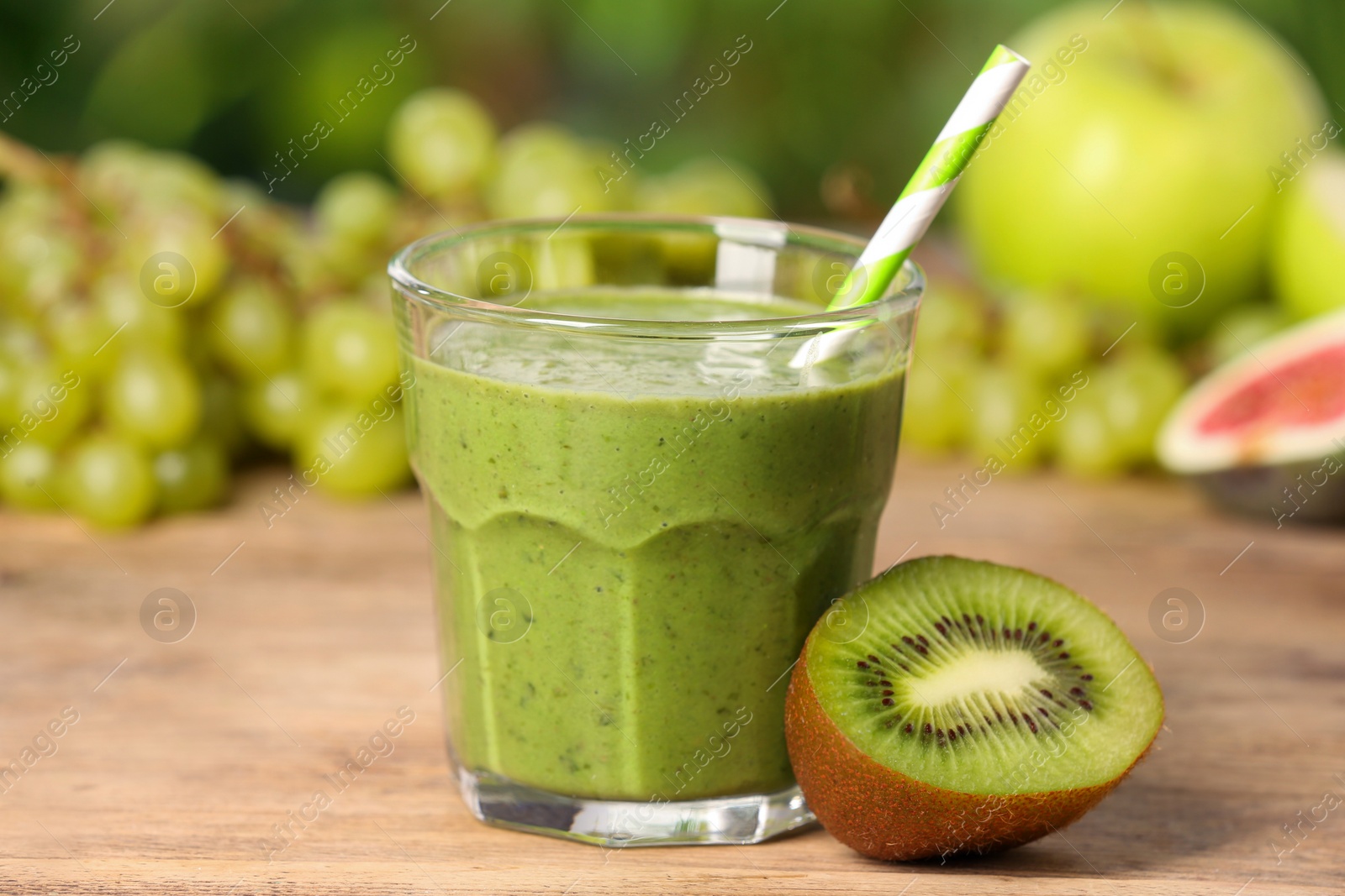 Photo of Glass of fresh green smoothie and ingredients on wooden table outdoors