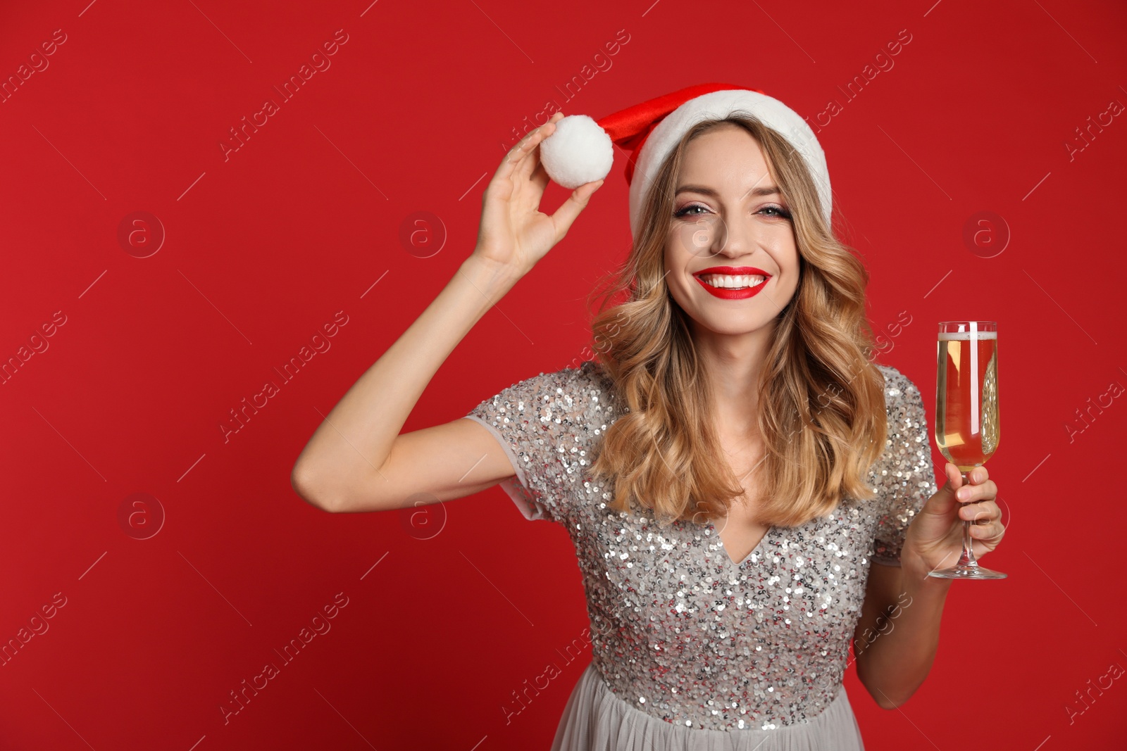 Photo of Happy young woman wearing Santa hat with glass of champagne on red background. Christmas celebration