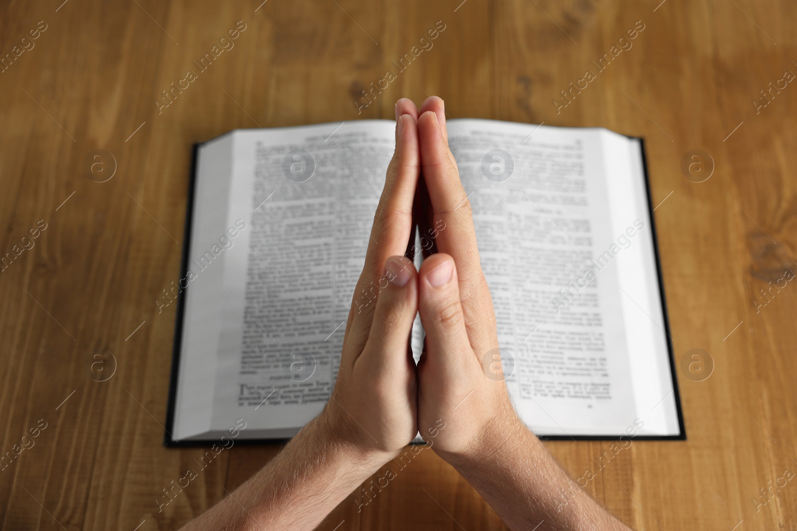 Photo of Man with Bible praying at wooden table, closeup