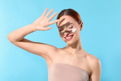 Photo of Beautiful young woman shading herself with hand from sunlight on light blue background