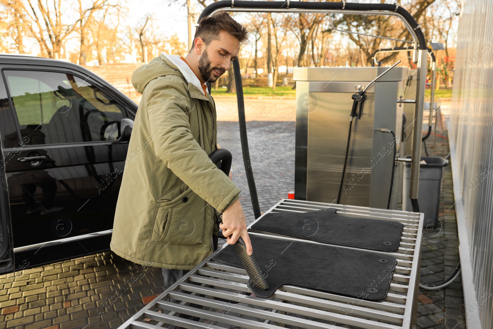 Photo of Man cleaning auto carpets with vacuum cleaner at self-service car wash