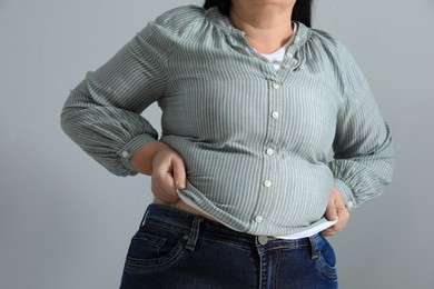 Photo of Overweight woman in tight shirt on light grey background, closeup