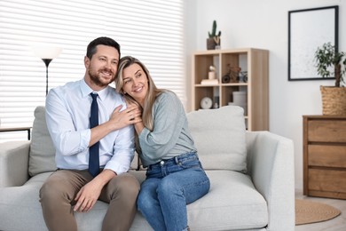 Happy couple sitting on sofa at home, space for text