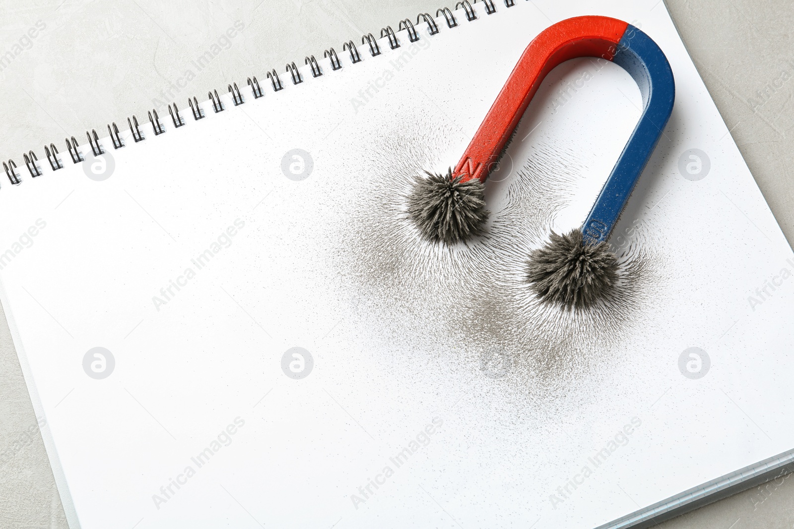 Photo of Magnet with iron powder on notebook, top view. Space for text