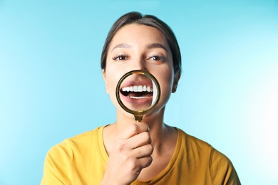 Photo of Young woman with healthy teeth and magnifier on color background