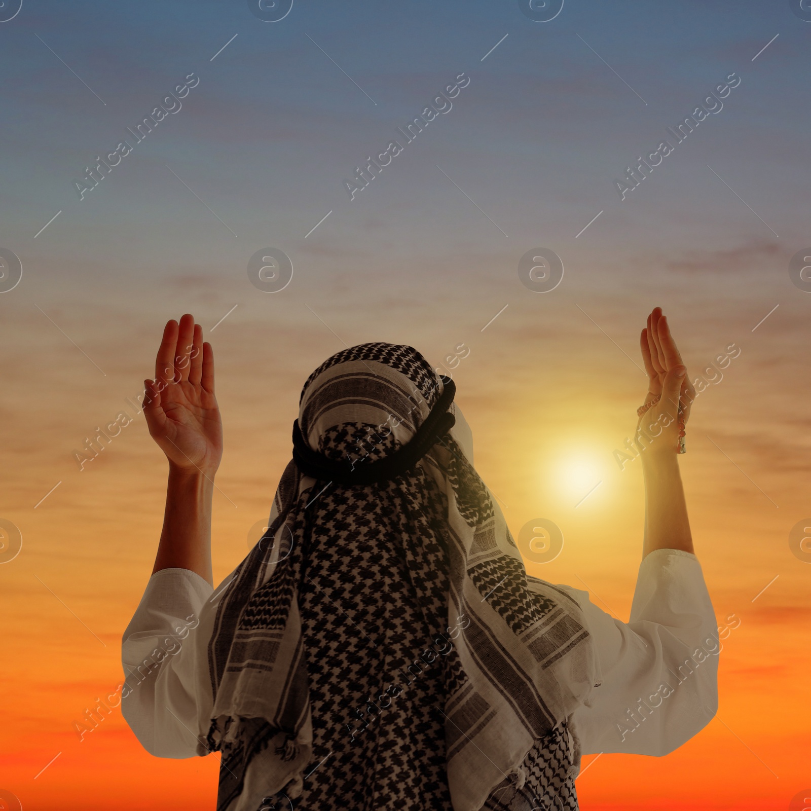 Image of Muslim man praying in traditional clothes outdoors at sunset