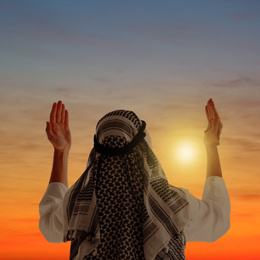 Image of Muslim man praying in traditional clothes outdoors at sunset