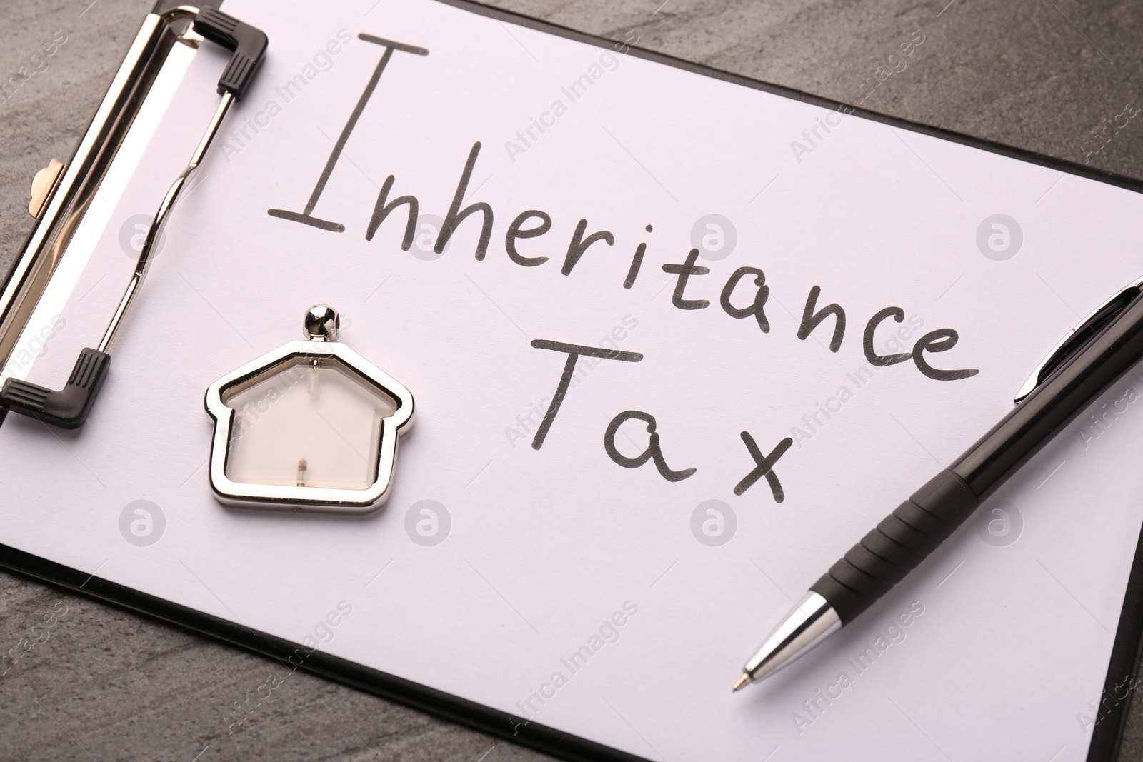 Photo of Inheritance Tax. Clipboard, pen and key chain in shape of house on grey table, closeup