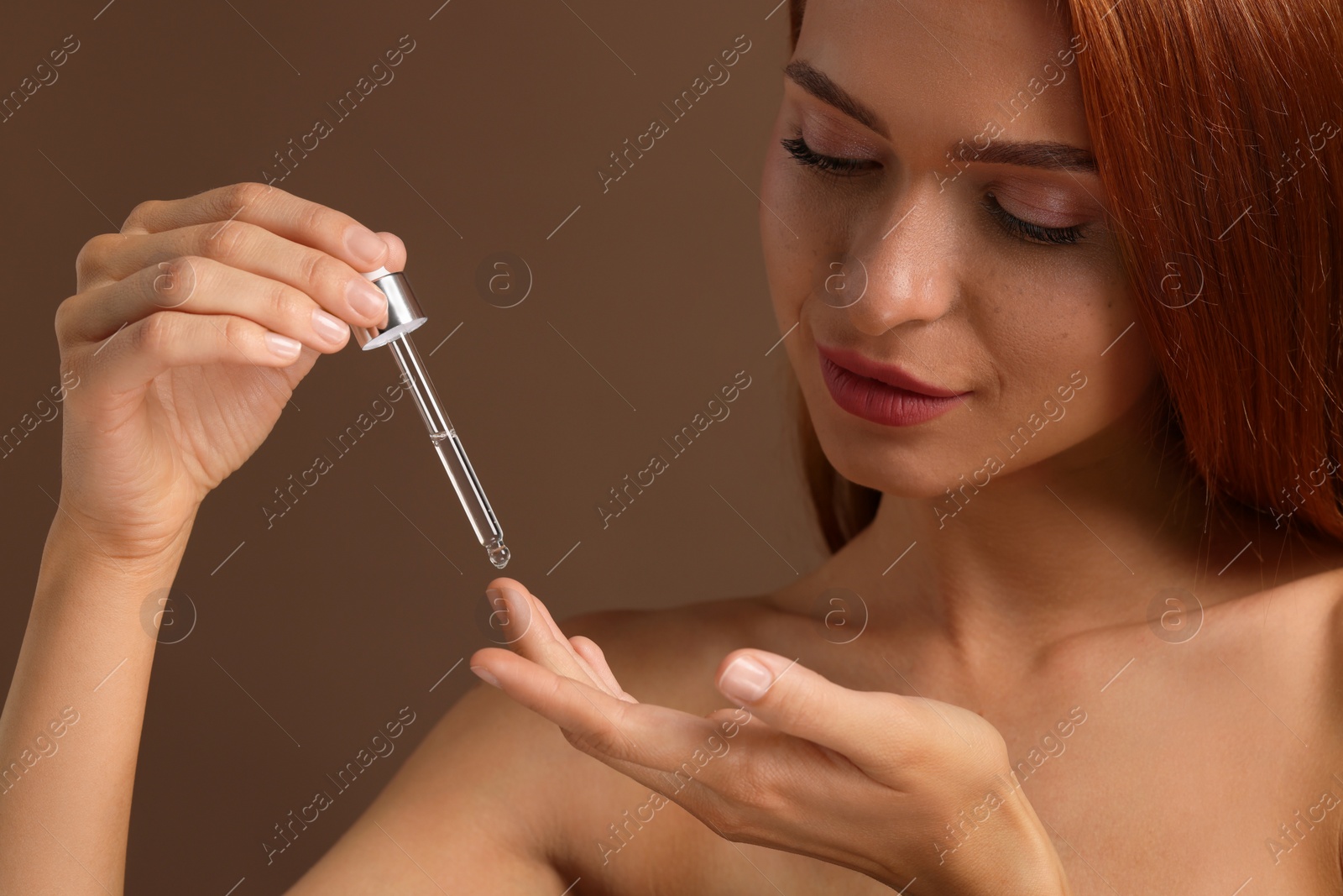 Photo of Beautiful young woman applying cosmetic serum onto her finger on brown background, closeup