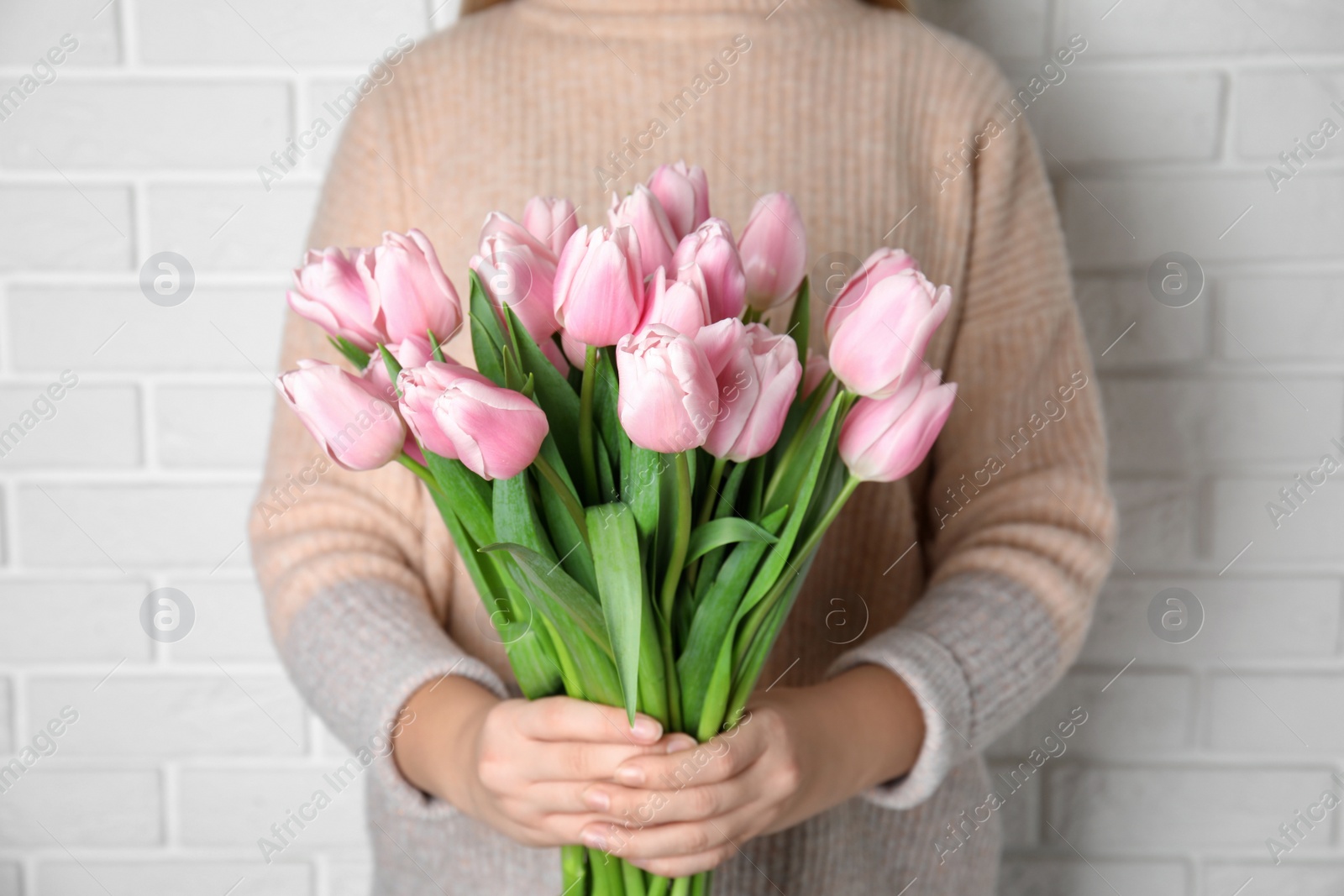 Photo of Woman with beautiful pink spring tulips near white brick wall, closeup