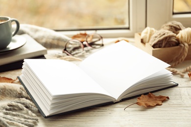 Photo of Open book and autumn leaves on windowsill. Space for text