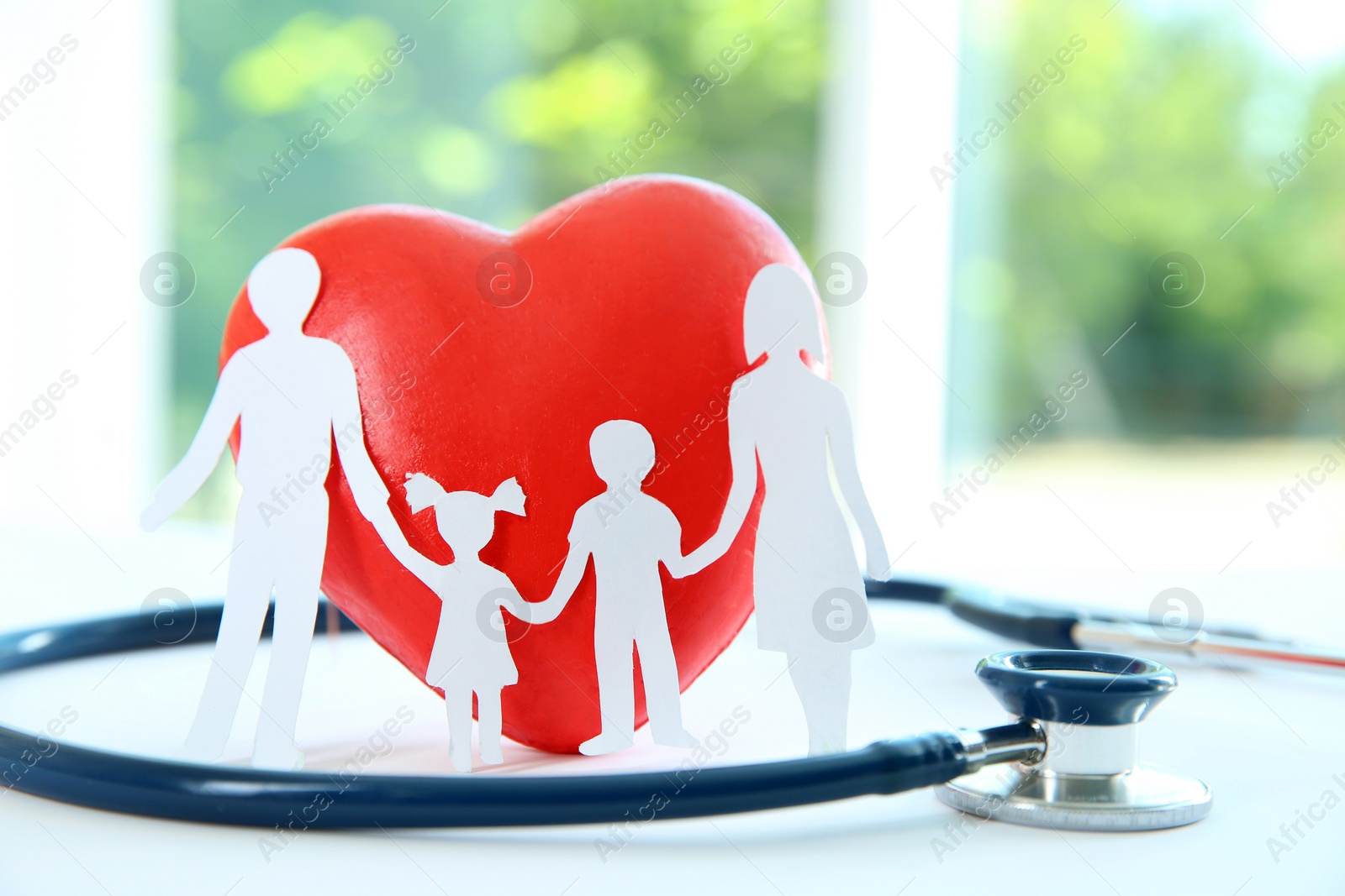 Photo of Red heart model, stethoscope and paper family cutout on table, closeup