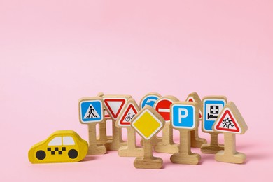 Photo of Set of wooden road signs and car on light pink background. Children's toy