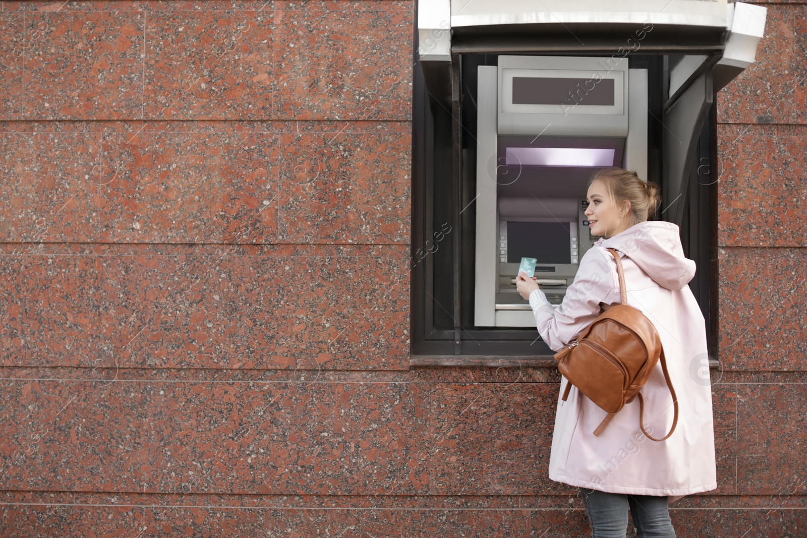 Photo of Young woman with credit card near cash machine outdoors. Space for text