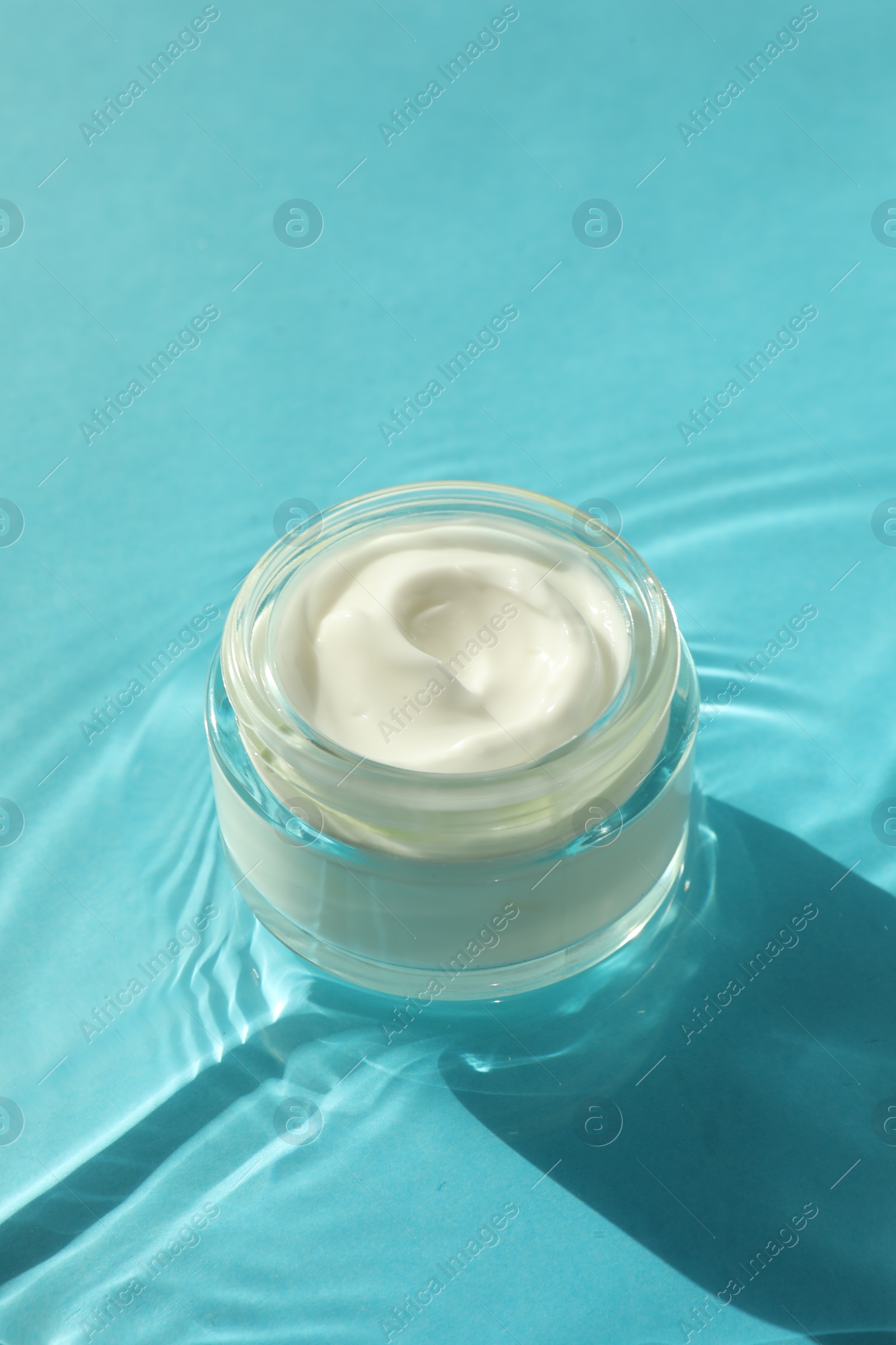 Photo of Jar with moisturizing cream in water on light blue background