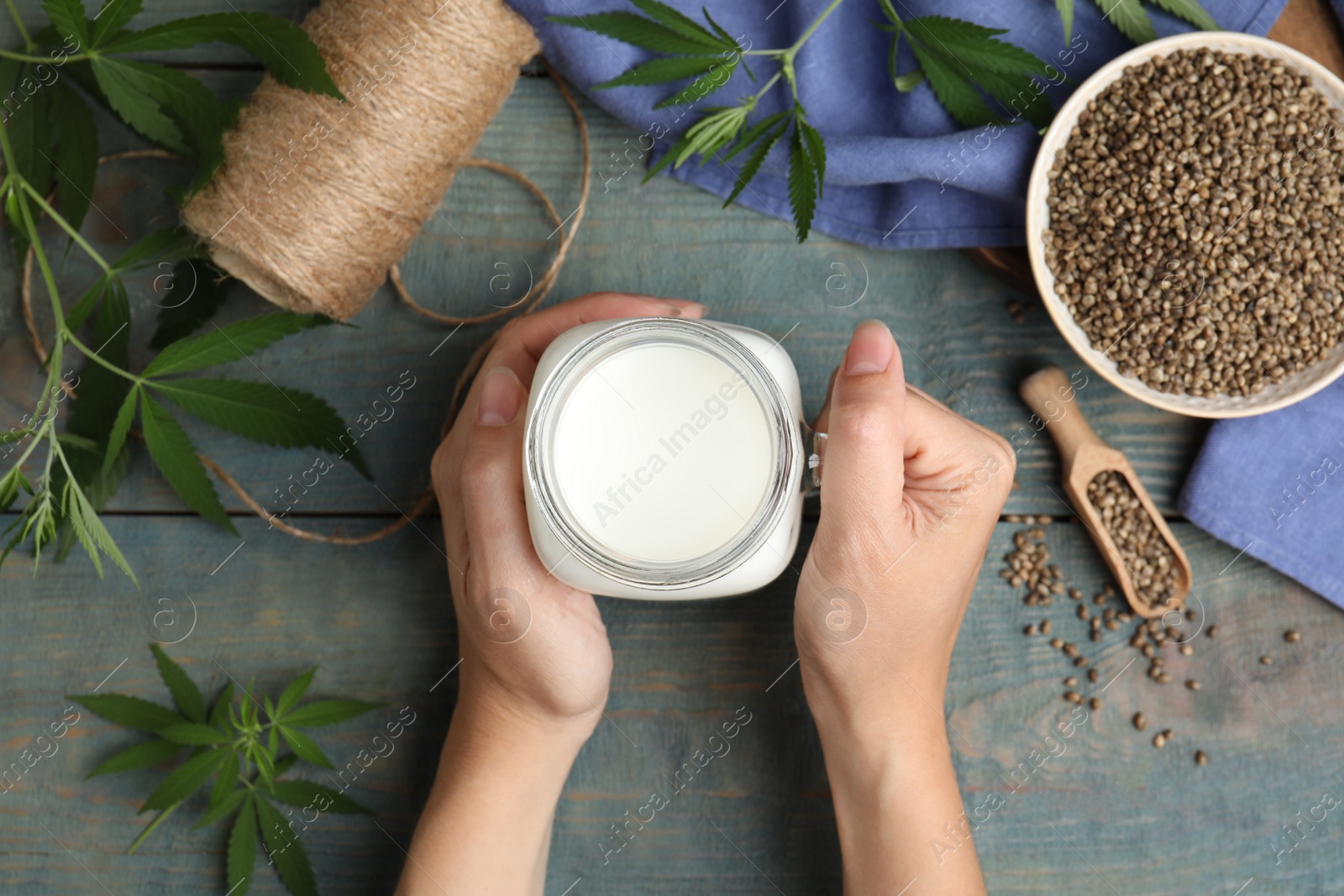 Photo of Woman with mason jar of hemp milk at light blue wooden table, top view