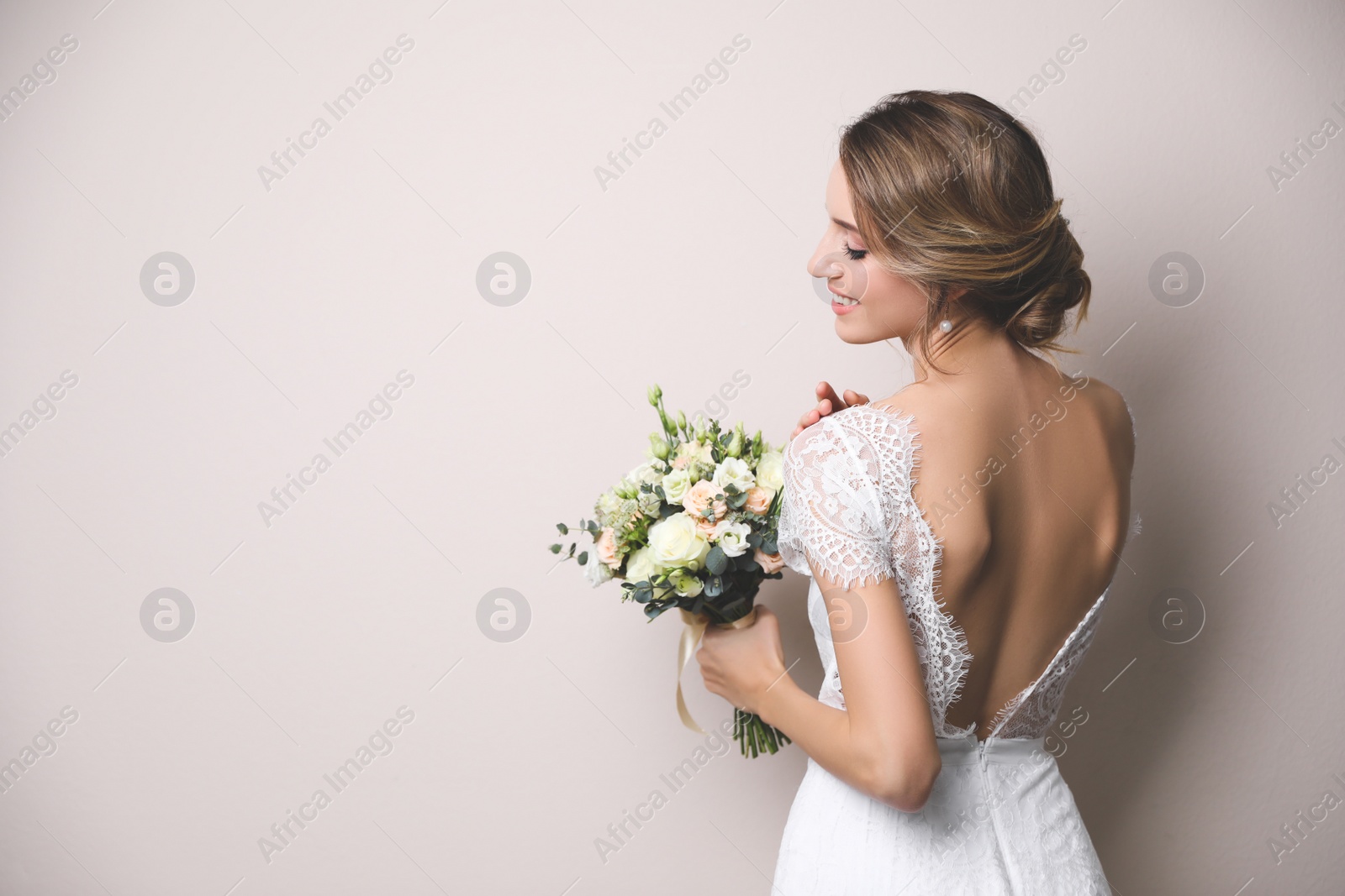 Photo of Young bride with elegant hairstyle holding wedding bouquet on beige background. Space for text