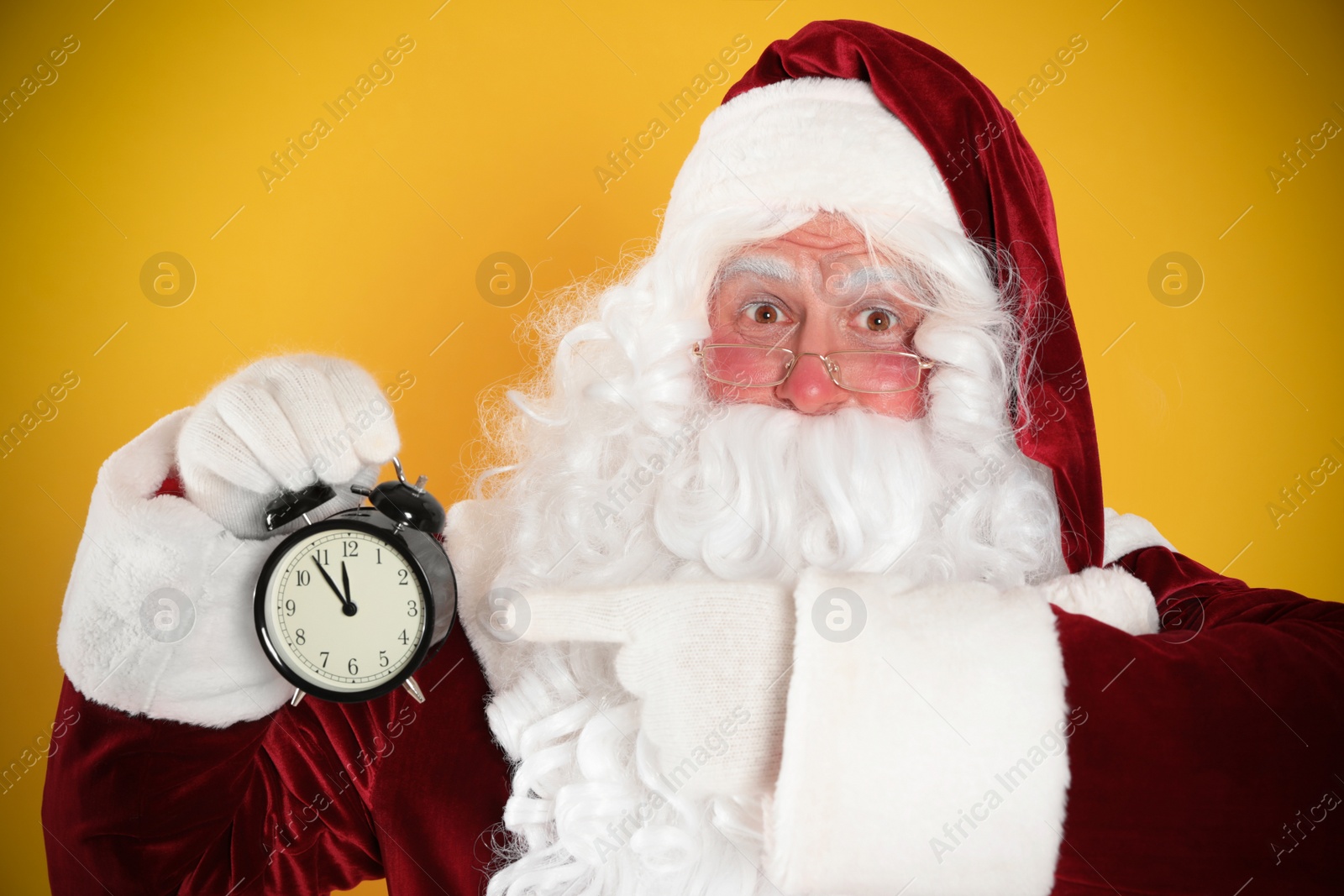 Photo of Santa Claus holding alarm clock on yellow background. Christmas countdown