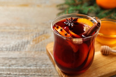 Photo of Glass cup of tasty mulled wine on wooden table. Space for text