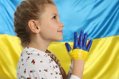 Photo of Little girl with clasped painted hands near Ukrainian flag