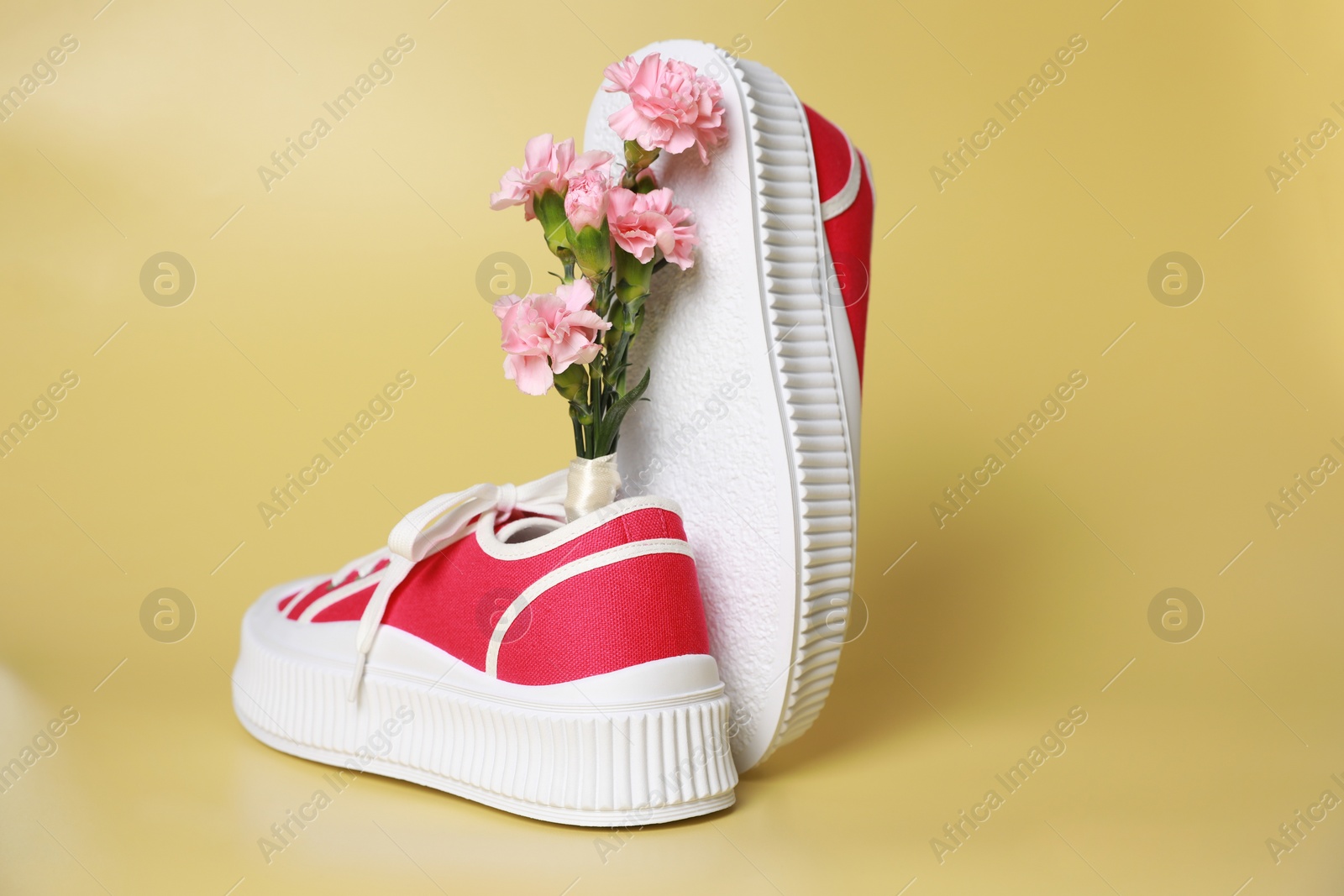 Photo of Pair of red classic old school sneakers and carnation flowers on yellow background