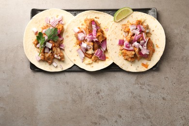 Delicious tacos with vegetables, meat and lime on grey textured table, top view. Space for text