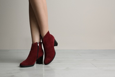 Woman wearing stylish boots near beige wall indoors, closeup. Space for text